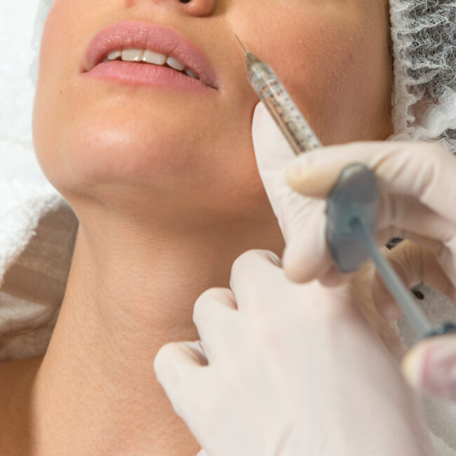 Cosmetic injection to the pretty caucasian woman face and beautician hands with syringe